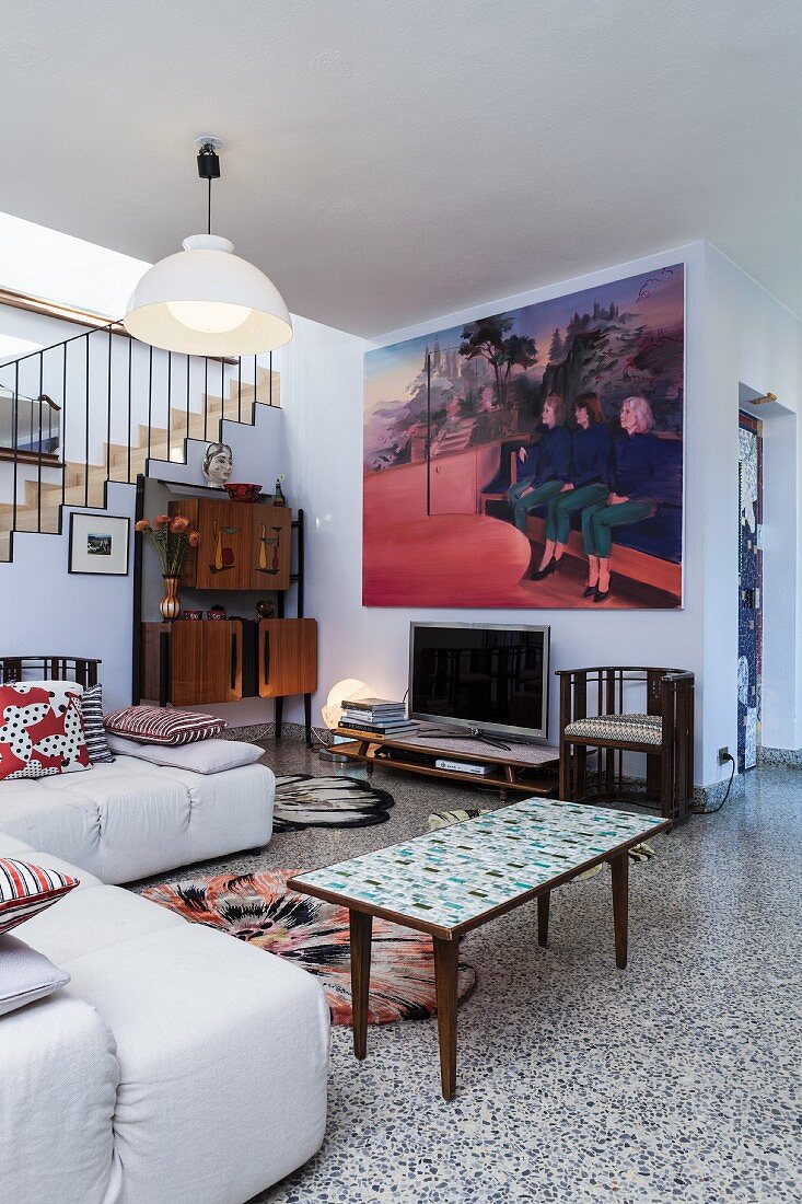 Modernes, helles Sofa und Retro Couchtisch auf Terrazzoboden, im Hintergrund modernes Bild an Wand in offenem Wohnraum