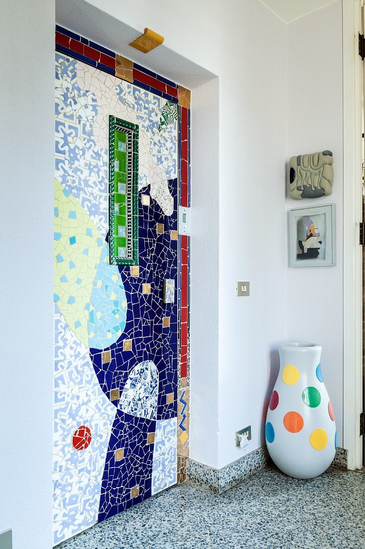 Künstlerisch gestaltete Wandnische mit bunten Fliesen, seitlich Bodenvase mit farbigen Punkten auf Terrazzoboden