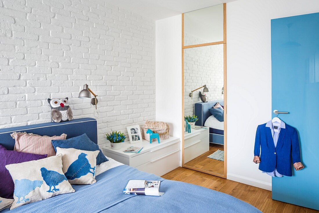 Doppelbett in Blautönen vor weiss geschlemmter Backsteinwand, raumhoher Ankleidespiegel im Schlafzimmer