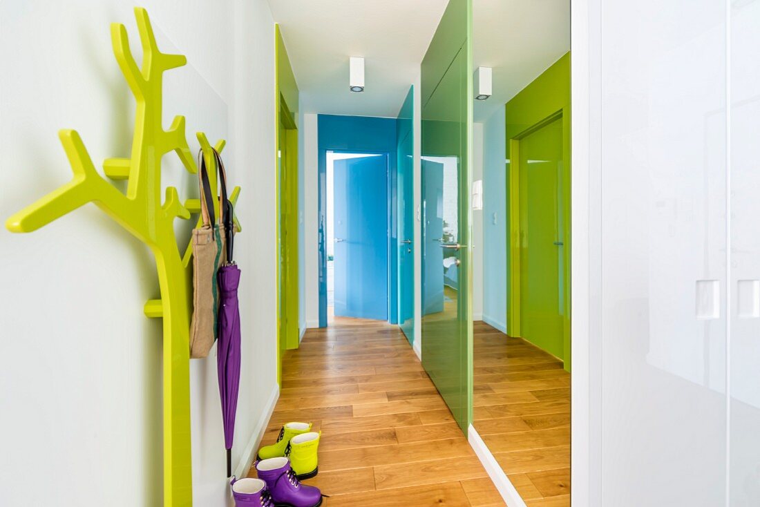 Gang mit seitlichem Spiegelfront, bunten Türfronten und grünem, stilisiertem Baum als Garderobe