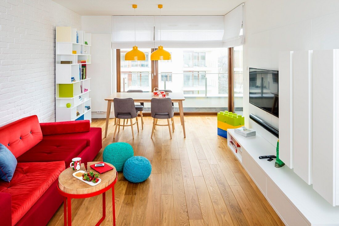 Long, open-plan interior with red sofa, media cabinet and dining area in background