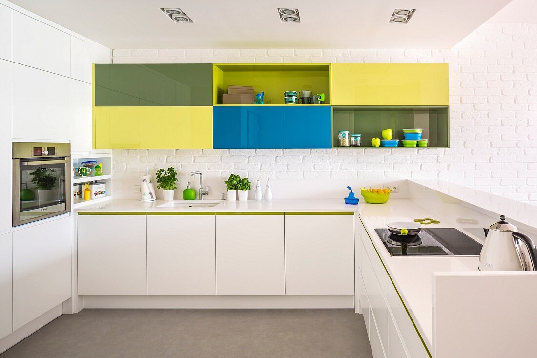 Colourful wall cabinets on white brick wall in modern, white fitted kitchen with raised counter
