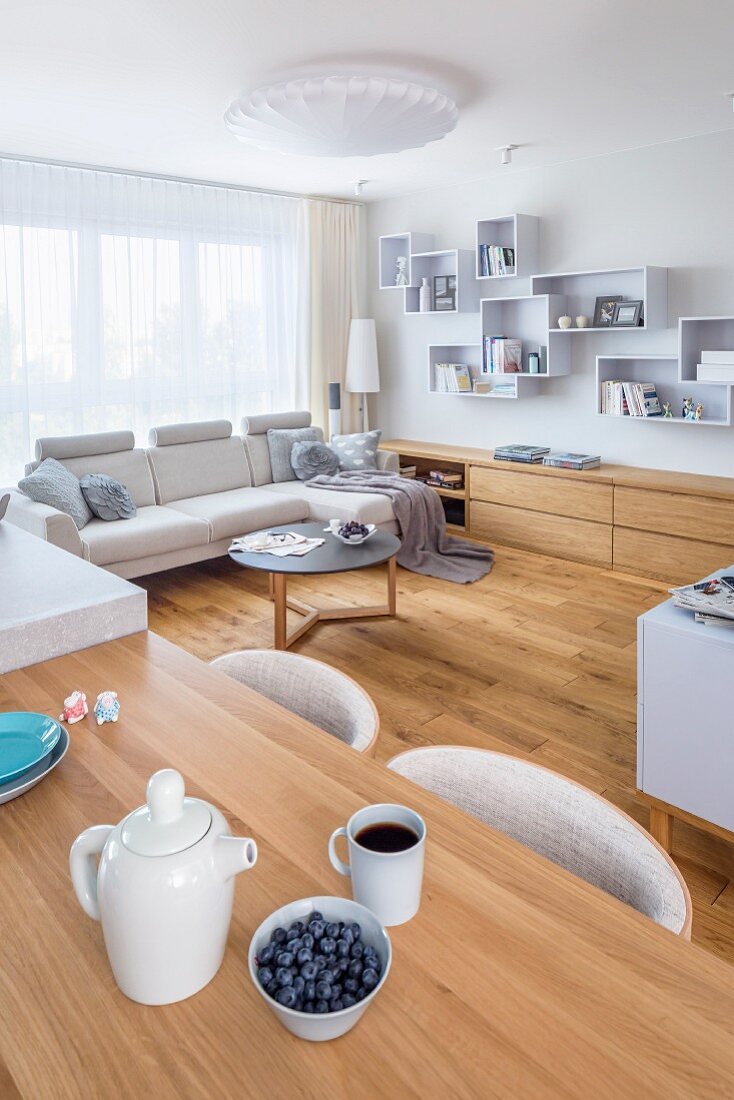 Offener Wohnraum mit schlichten Holzmöbeln und heller Polstergarnitur in kleinem Appartement