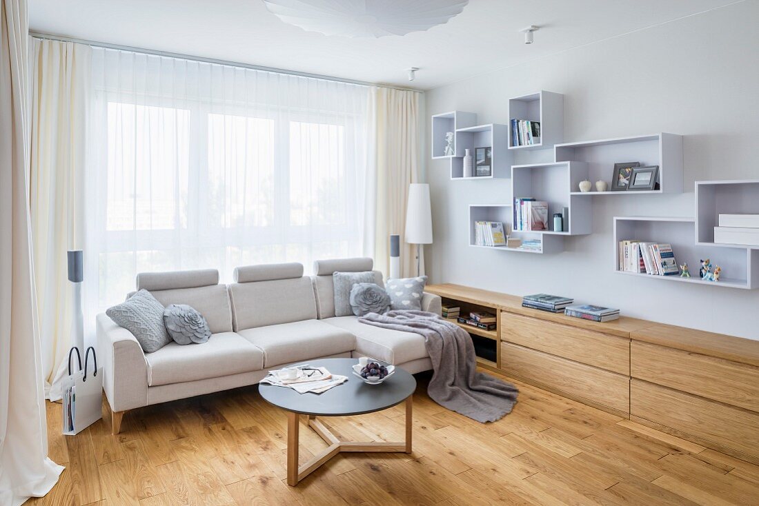 Helle Couch mit Coffeetable vor Fenster, neben eingebautem Sideboard und Systemregal aus Wandkästen