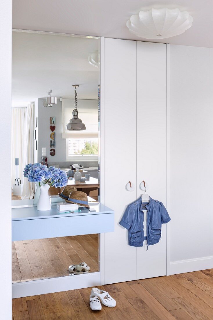 White fitted wardrobe with pale blue floating shelf and mirror in hallway
