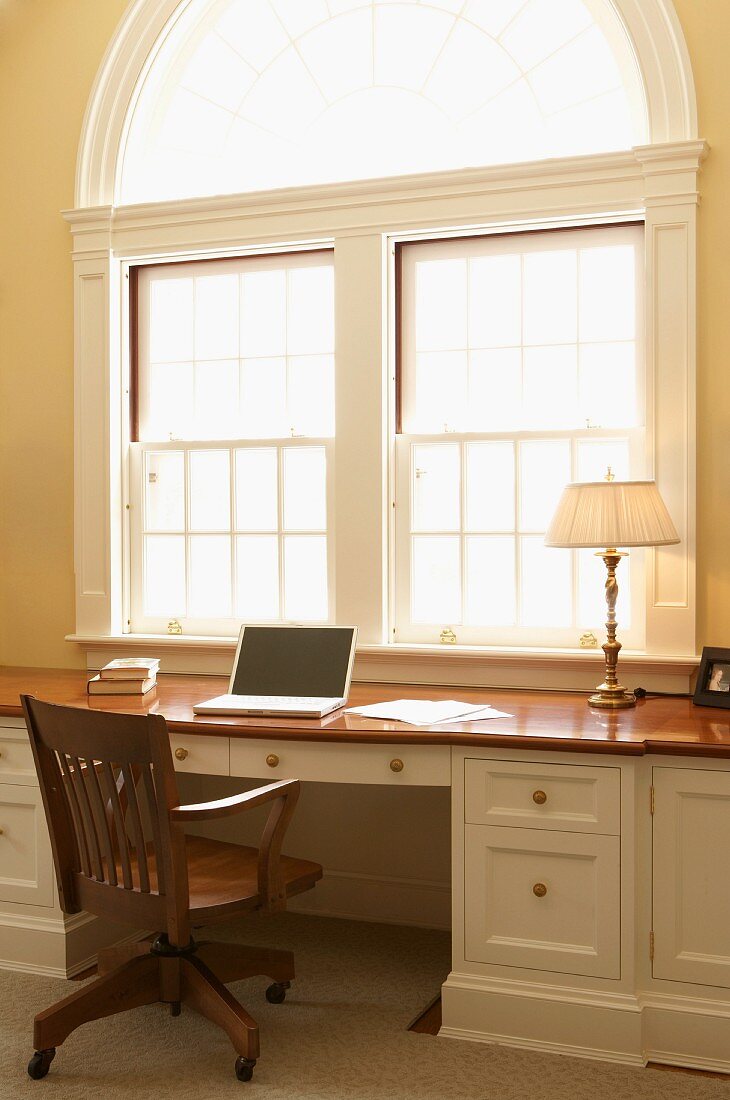Traditioneller Schreibtisch mit Laptop vor großem Rundbogenfenster