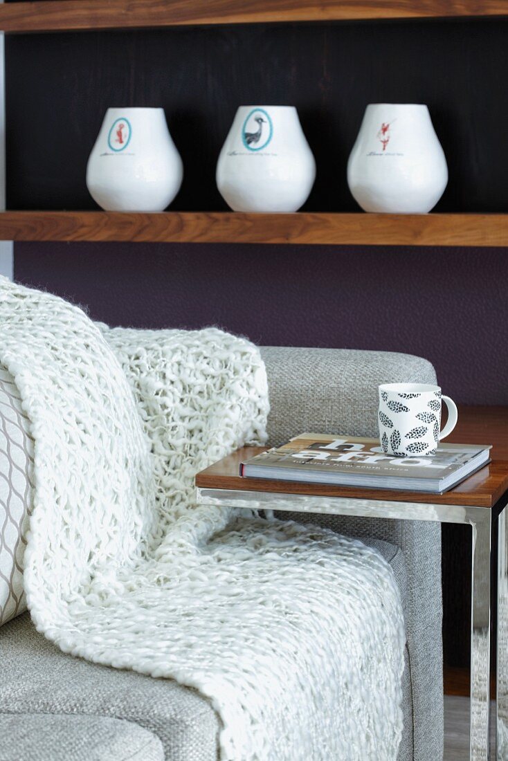 Minimalistischer Beistelltisch vor Couch, im Hintergrund Vasen auf Holzablage