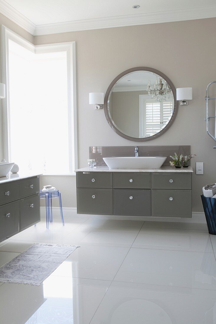 Elegantes Bad mit glänzendem Fussboden, Waschtisch mit grauem Schubladenschrank und rundem Wandspiegel