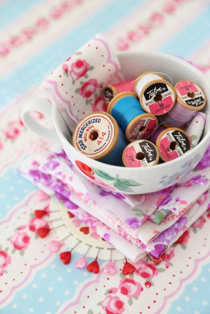 Old reels of cotton in china cup on floral fabric