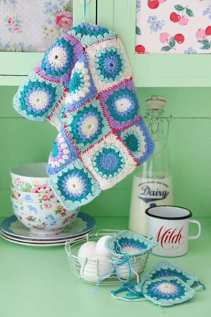 Pastel crochet patchwork - doilies on pale green kitchen dresser with vintage crockery and basket of eggs
