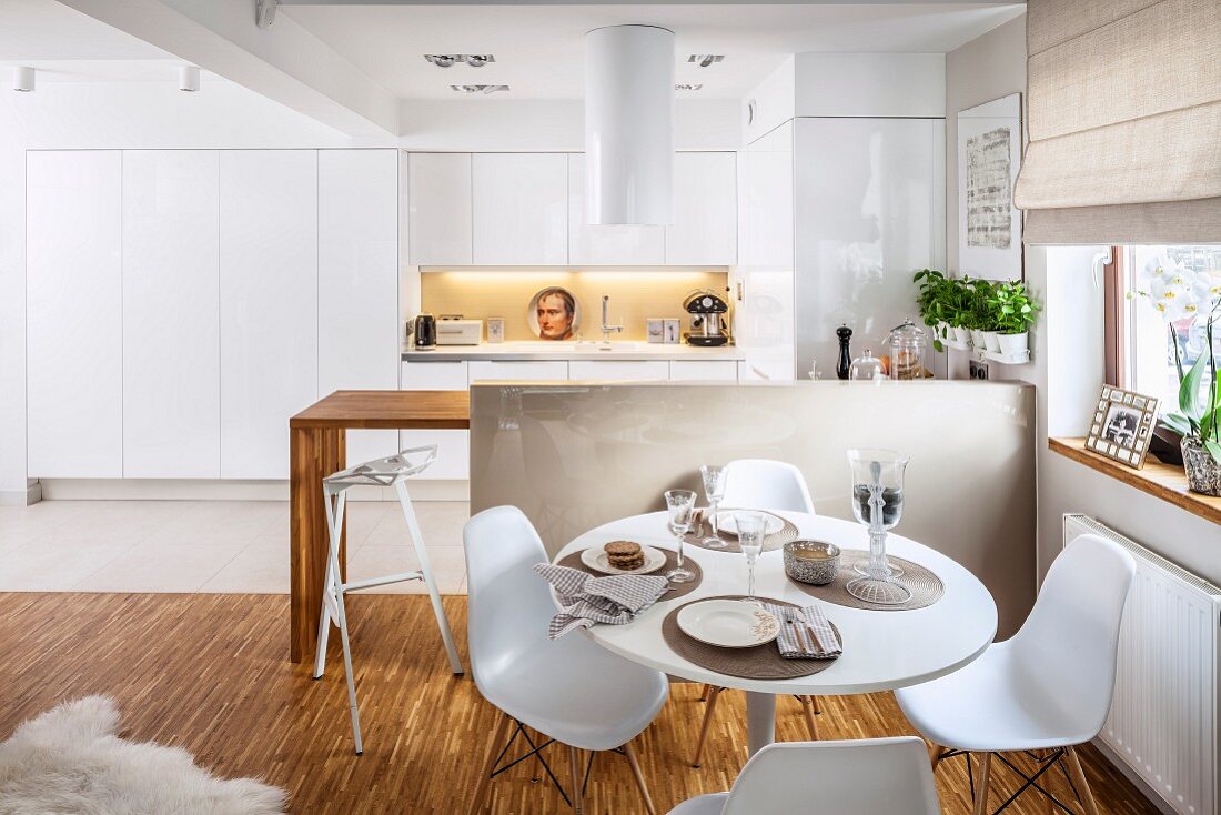 Place settings on Tulip Table and Plastic Chairs in front of breakfast bar in open-plan fitted kitchen