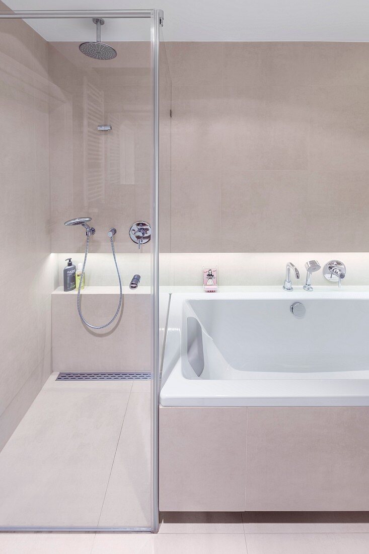 Walk-in shower with glass partition wall next to bathtub; continuous shelf in niche with indirect lighting