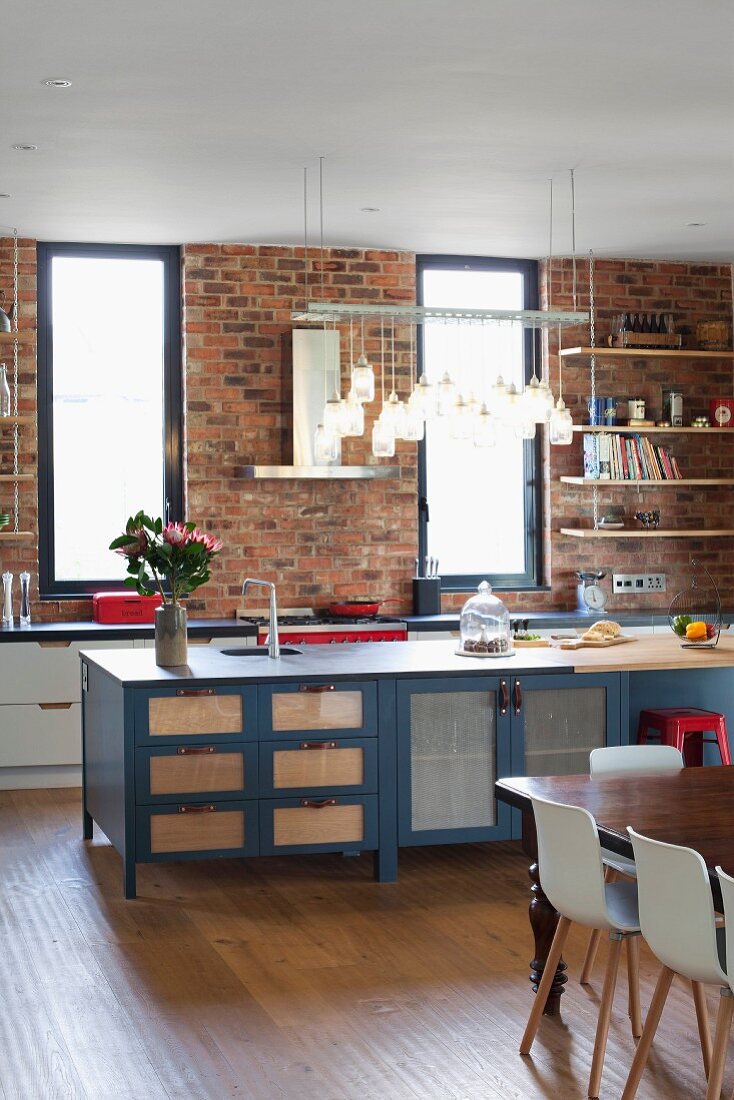 Row of lights above island counter with ample storage space and kitchen counter against brick wall