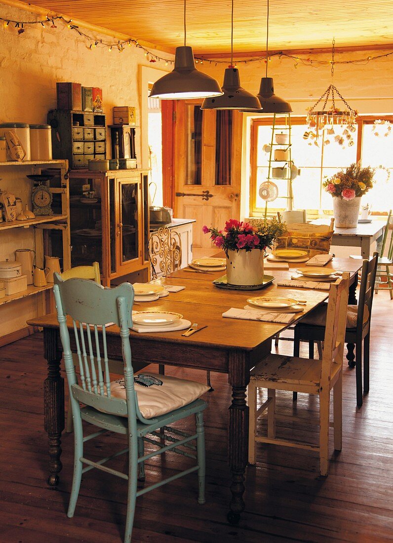 Gedeckter Esstisch mit Holzstühlen, oberhalb Vintage Pendelleuchten in Reihe in bäuerlicher Küche