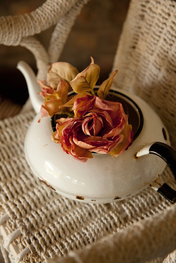 Vintage Teekanne aus weißem Emaille mit Rosen auf Korbsttuhl