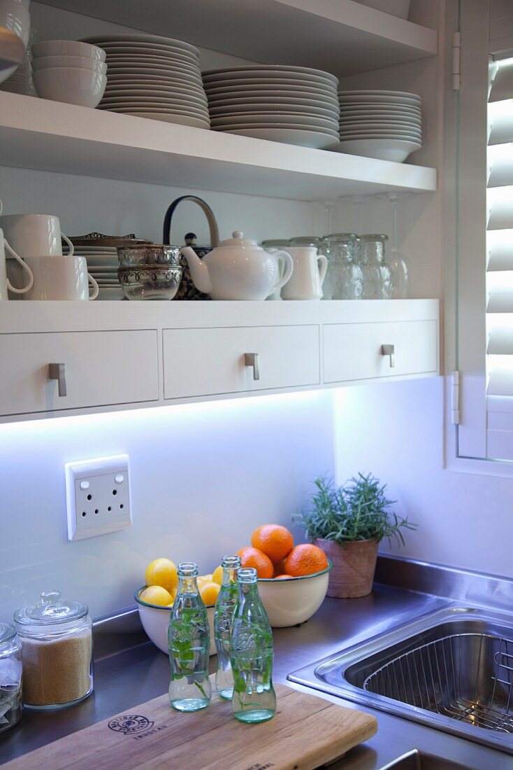 Ausschnitt einer Küche, weisses Geschirr auf Regalböden, teilweise mit integrierten Schubläden, über Küchenzeile