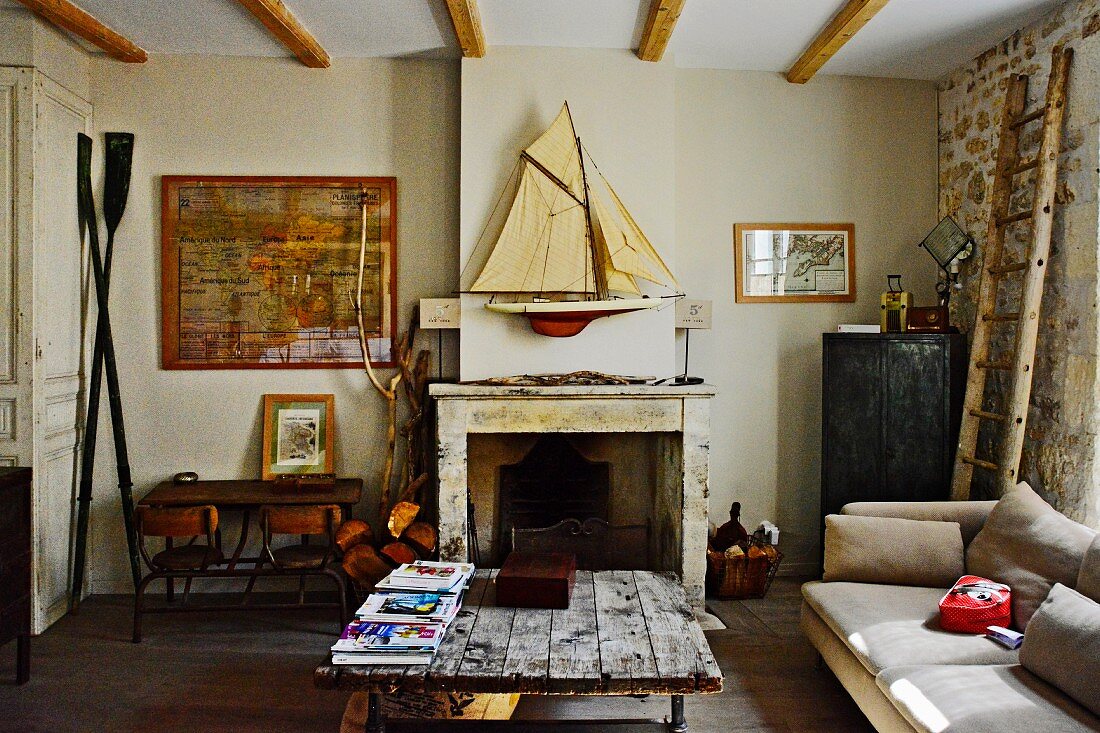 Rustic coffee table with board top and open fireplace below model sailing boat on wall in simple living room