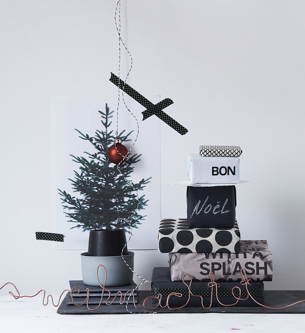 Stack of gifts wrapped in black and white paper next to printed picture of Christmas tree