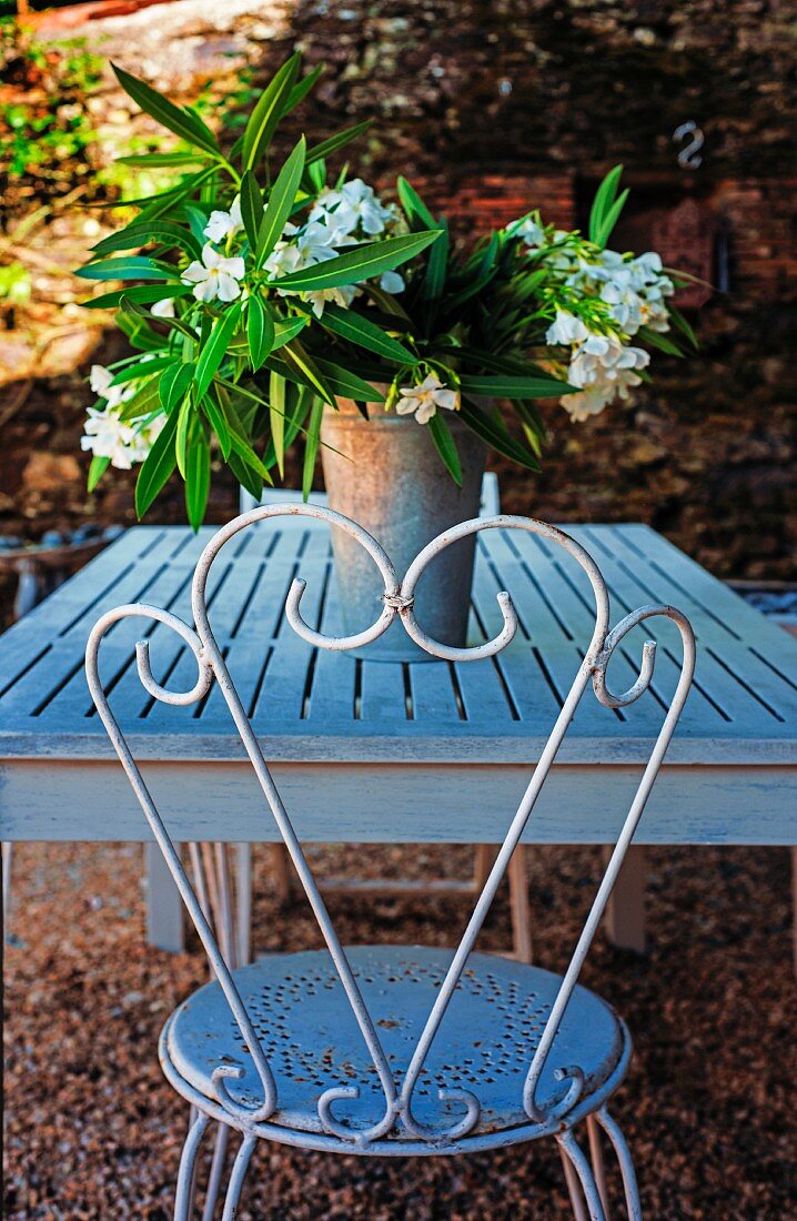 Metallstuhl am Gartentisch mit weiss blühendem Oleander