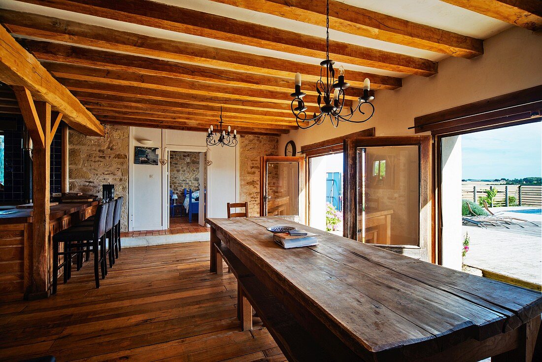 Lange Holztafel vor Terrassentüren in offener Küche mit Holzbalkendecke, in mediterranem Landhaus
