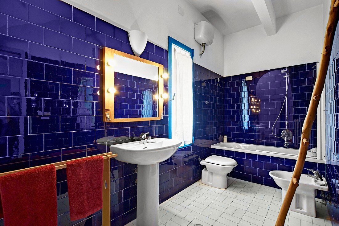 Glossy, ultramarine wall tiles in Mediterranean-style bathroom with bathtub, pedestal sink and bidet