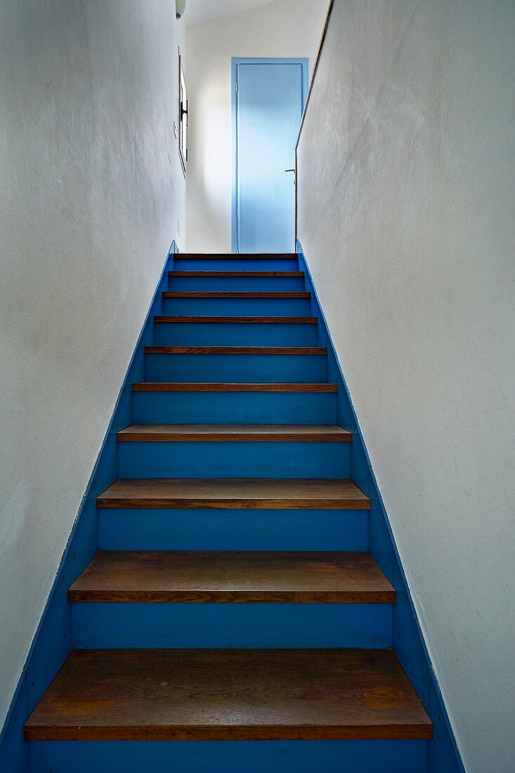 Blau gestrichene Holztreppe mit naturbelassenen Trittstufen zwischen weißen Wänden und südländischem Charme