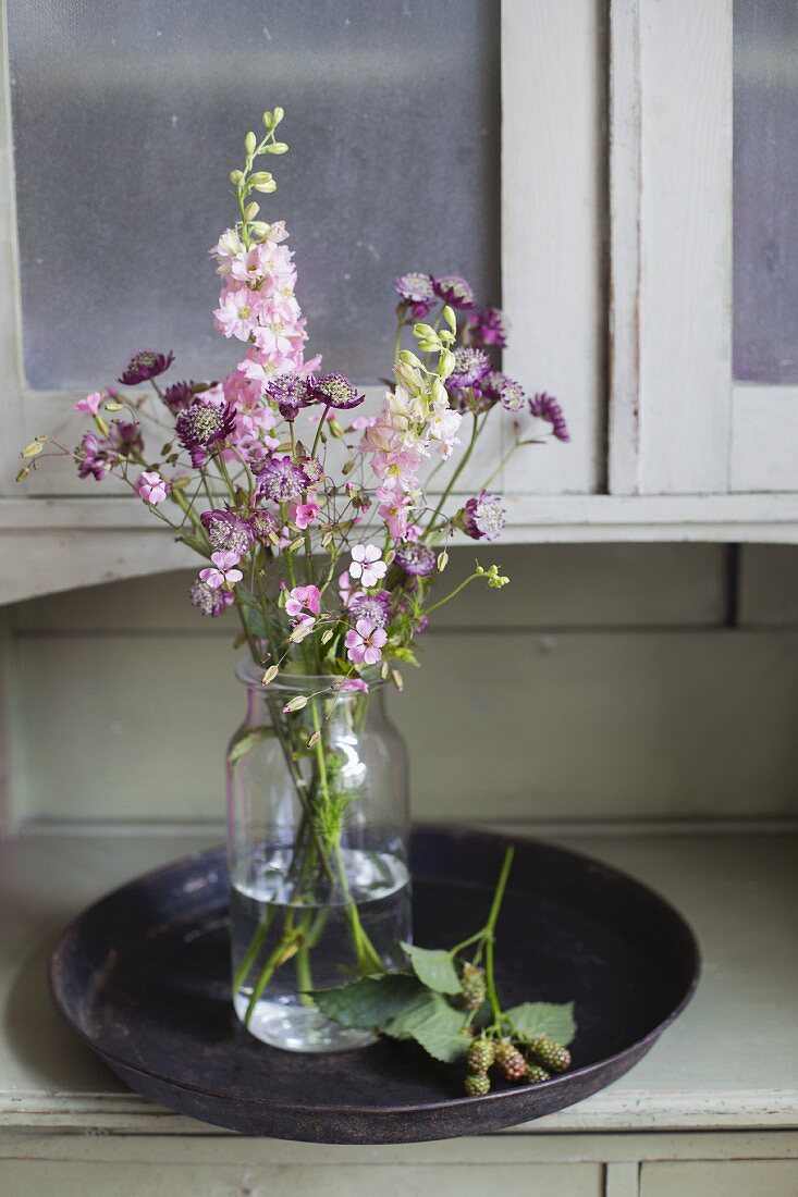 Pink delphiniums, astrantia and small pink flowers in jar of water on tray