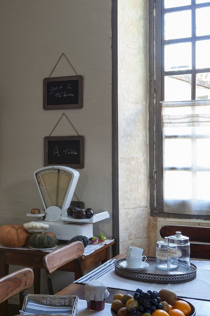 Mediterrane Küche mit antiker Waage, einem Sprossenfenster und einem Holztisch mit Obstschale
