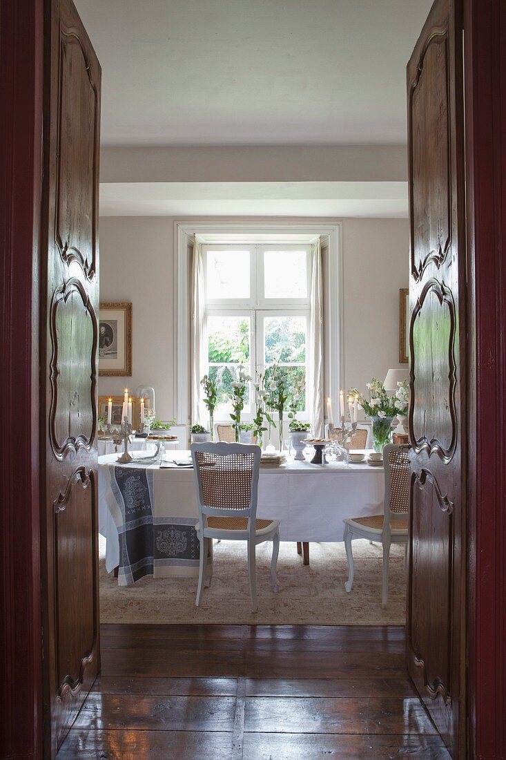 View through open double doors into dining room with antique furniture and festively set table