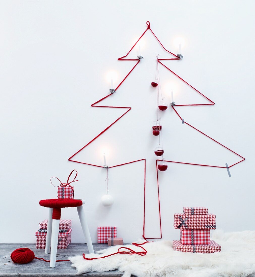 Silhouette eines Weihnachtsbaums aus rotem Wollgarn an der Wand, Hocker mit Wolle umwickelt