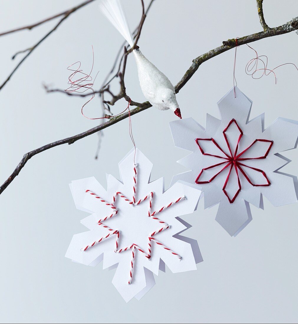 Paper snowflakes with embroidered details and bird ornament on bare branch