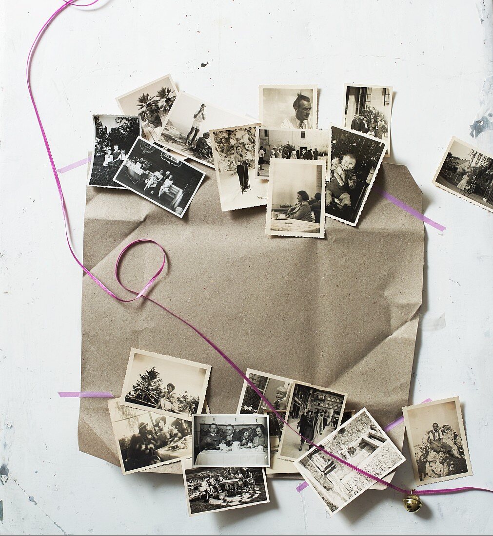 Alte, schwarz-weiße Familienfotos mit Geschenkband auf Packpapier als Weihnachtsdeko