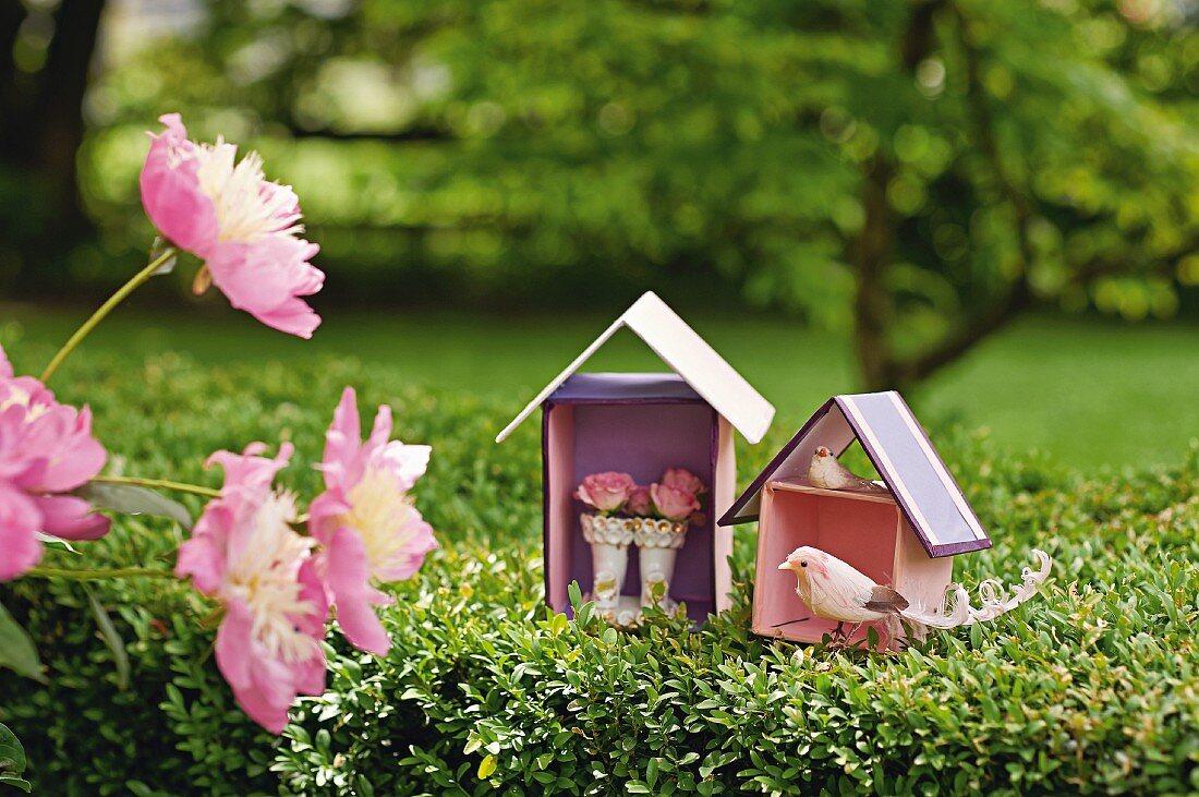 Bird figurine and roses in wto hand-crafted cardboard houses in garden