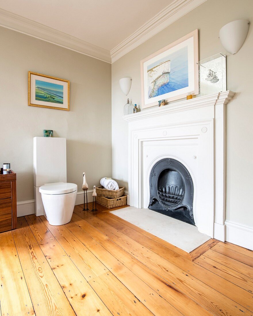 Modern toilet next to open fireplace in corner of bathroom with walls painted pale grey