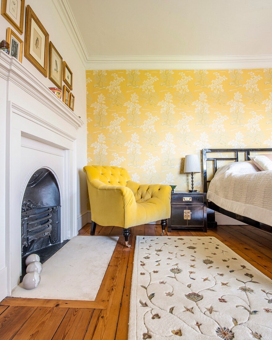 Kamin und antiker Sessel mit goldgelbem Bezug, vor tapezierte Wand mit floralem Muster auf gelbem Grund im Schlafzimmer