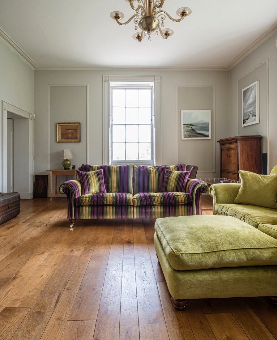 Polsterhocker vor Couch und elegantes Sofa mit Streifenbezug in grossräumigem Wohnzimmer