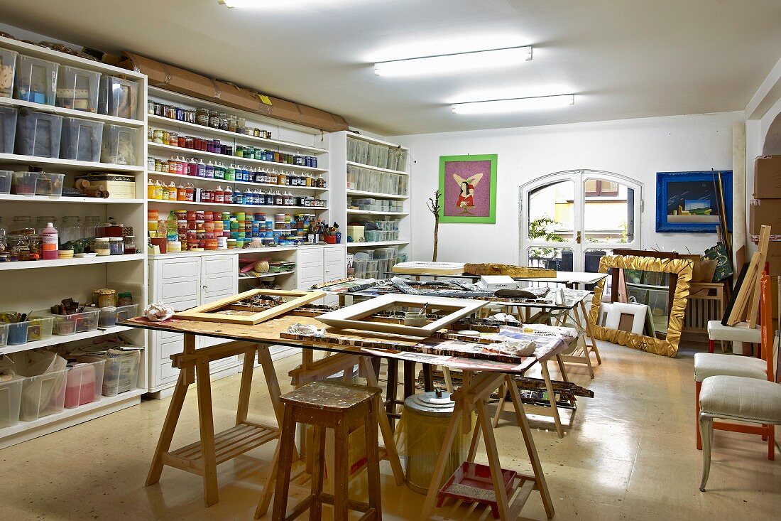 Regalwand mit Farbdosen und Kunststoffboxen in Künstlerwerkstatt mit diversen Holzrahmen