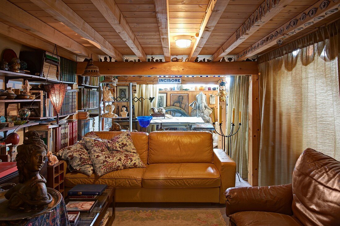 Pale brown leather couch in rustic interior with wooden ceiling and sculptor's workshop in background
