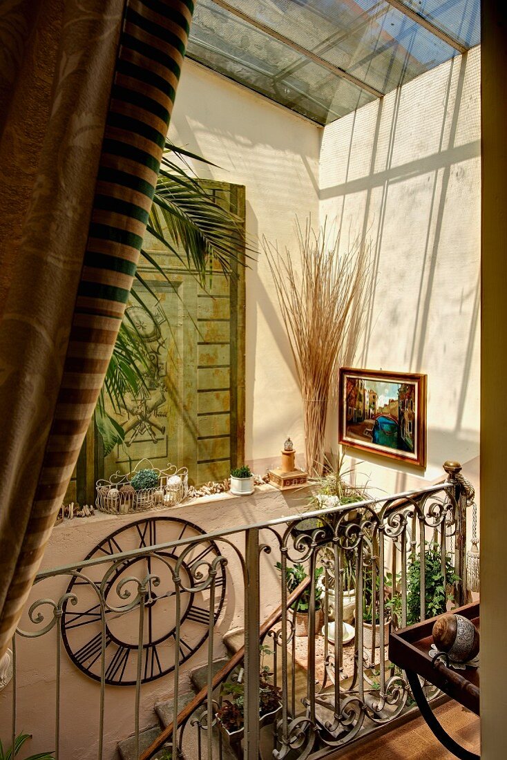 Glasdach mit Sonneneinfall in mediterranem Treppenhaus, schmiedeeisernes Geländer an Treppe, auf Sims Sammelsurium