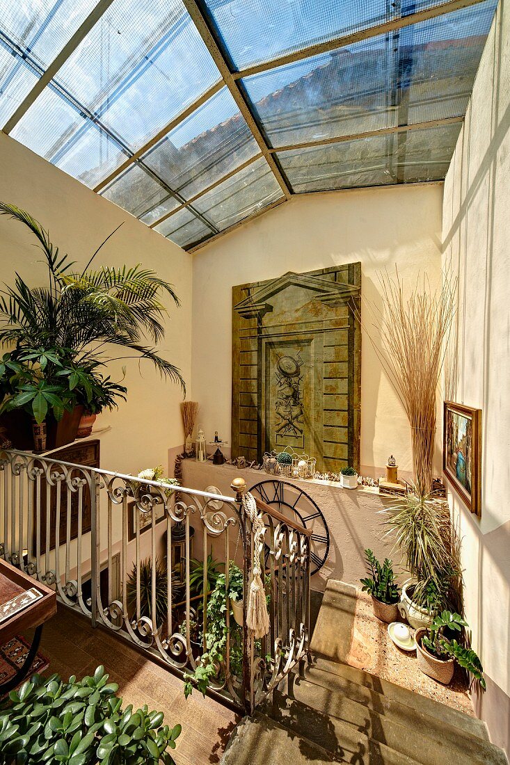 Sonnenbeschienenes Treppenhaus mit Glasdach, auf Boden und Ablagen Blumentöpfe in mediterranem Ambiente