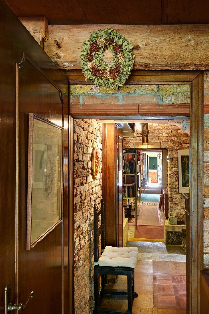 Kranz an Holzbalken über offener Tür und Blick in rustikalen Wohnraum, sichtbare Ziegelwand