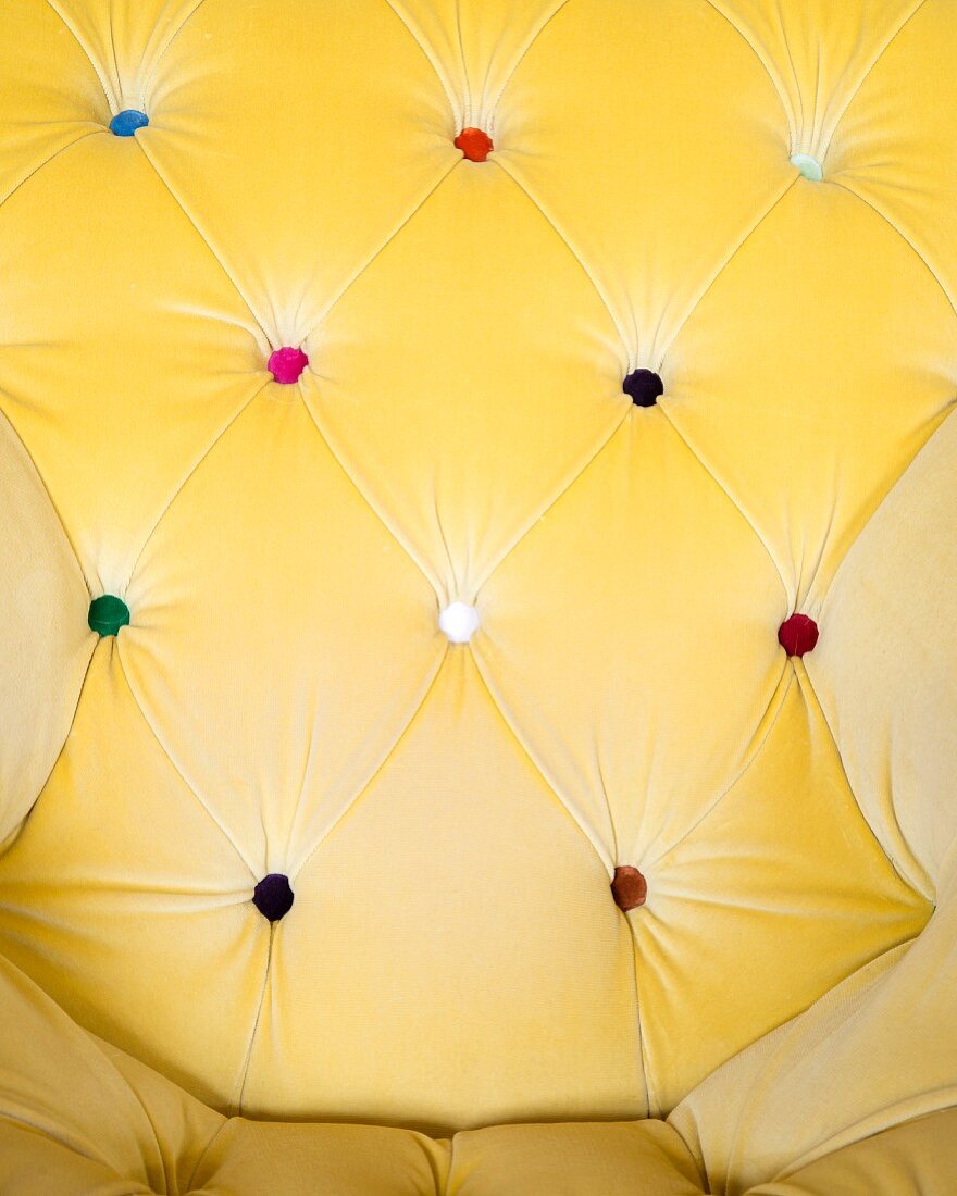 Backrest of button-tufted armchair upholstered in yellow fabric with buttons of various colours