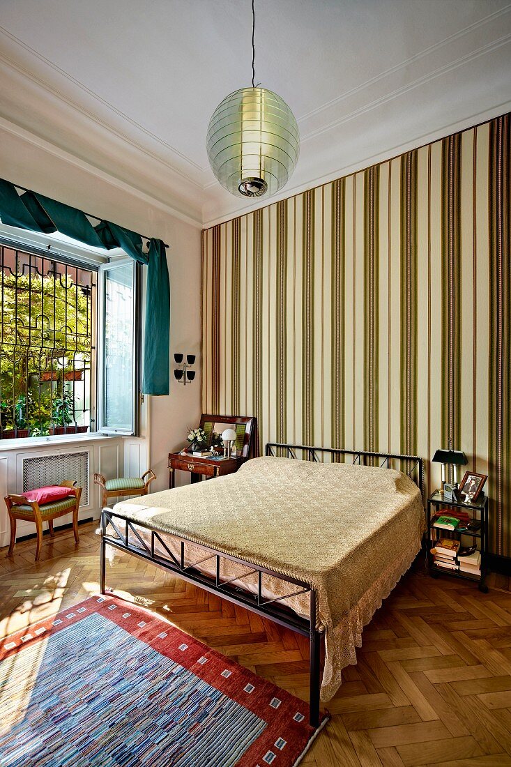 Doppelbett mit modernem Metallgestell vor Wand mit vertikaler Streifentapete in Schlafzimmer mit traditionellem Flair