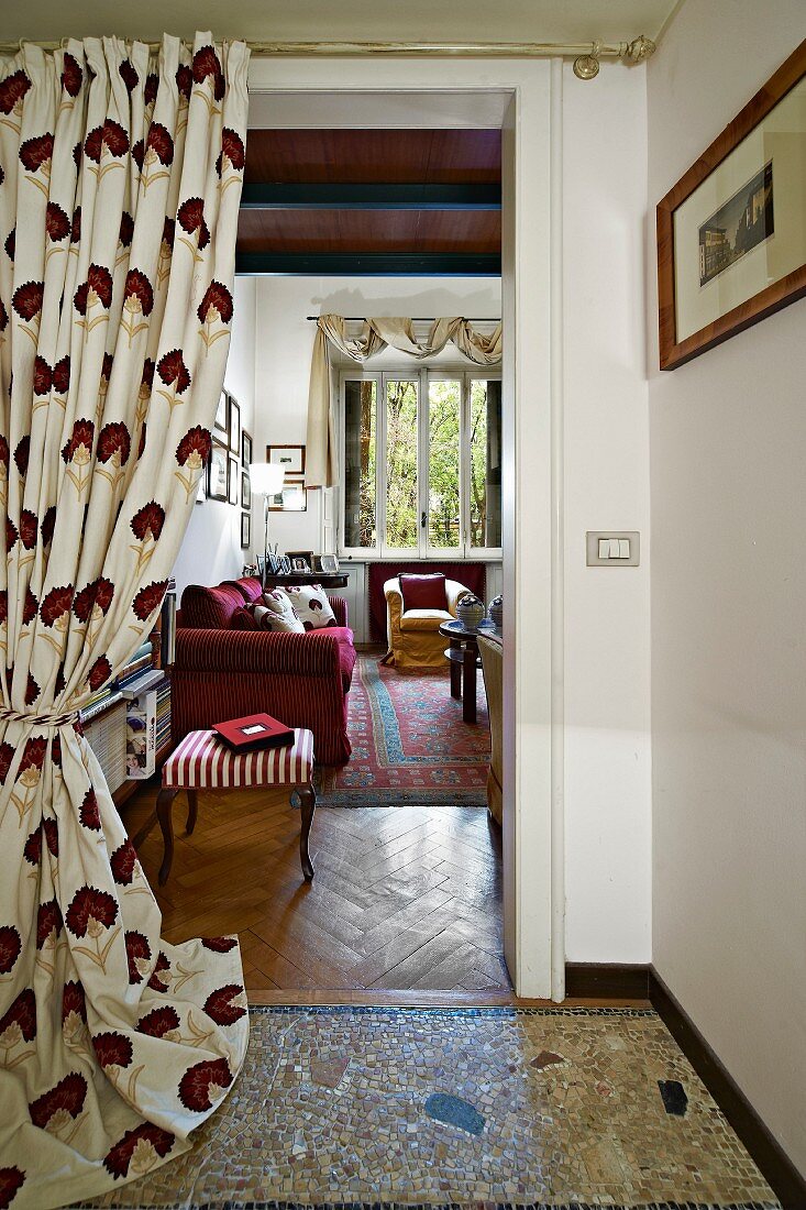 Gathered curtain on open doorway with view into living room with antique footstool and dark red couch