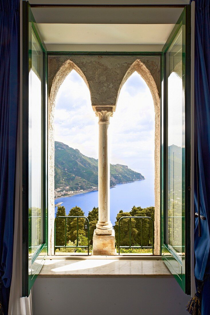 Façade element with pointed arches and Corinthian column behind open window with view of coastal landscape (Villa Cimbrone Hotel)