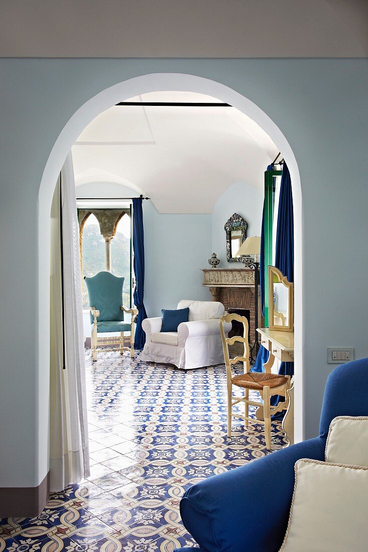 Blick vom Vorraum durch Rundbogen, auf hellen Sessel im Zimmer, mit durchgehendem Fliesenboden und Ornament Muster (Villa Cimbrone Hotel)