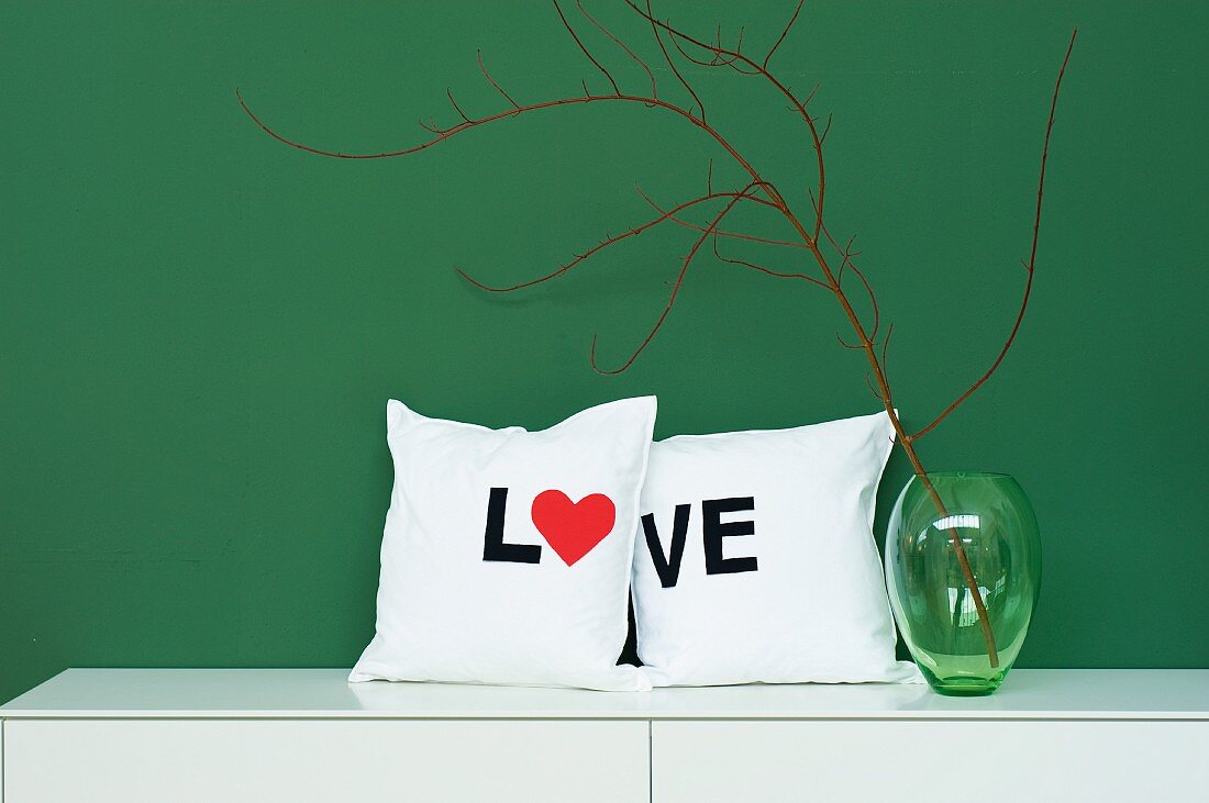 Selbst genähte Dekokissen mit 'LOVE' Schrift neben grüner Glasvase
