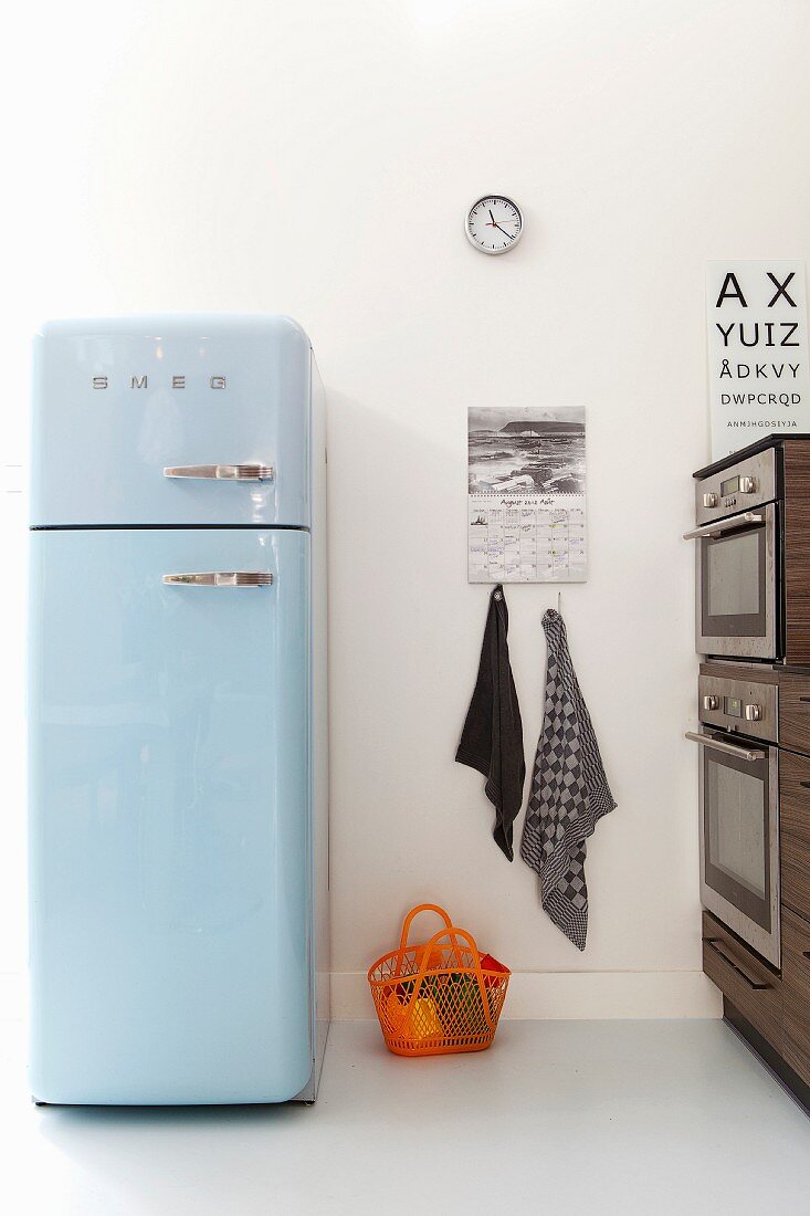 Hellblauer Retro-Kühlschrank in moderner Küche, am Boden orangefarbener Plastikkorb