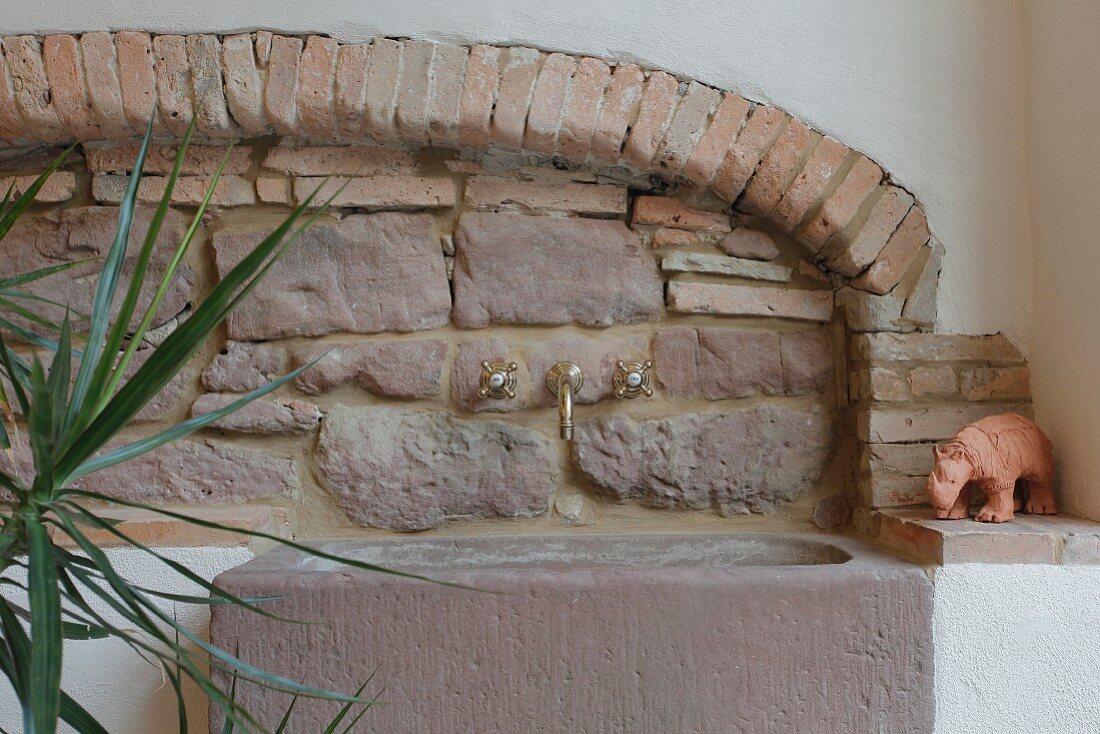 Rustikale Natursteinwand aus Sandstein und Backstein, Steinwaschbecken mit nostalgischen Armaturen