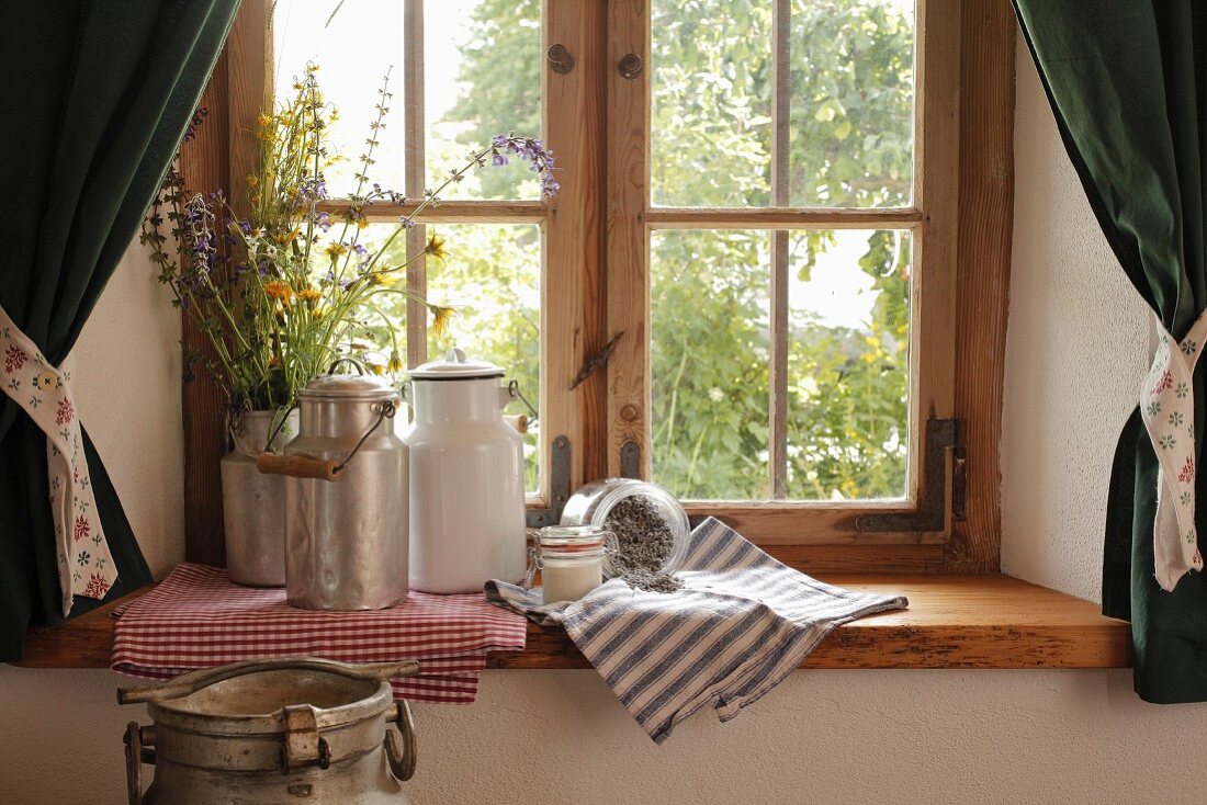 Vintage milk cans and jug of wild flowers on windowsill